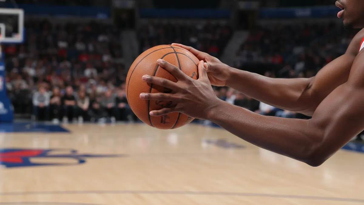 Manos de jugador de baloncesto sosteniendo el balón en la cancha.